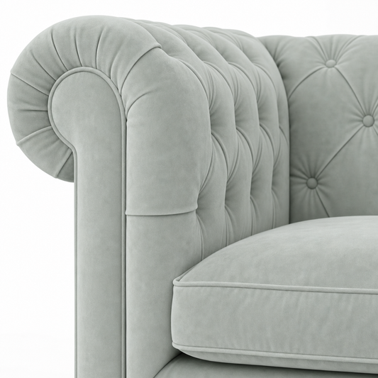 Close-up of a light blue tufted velvet armchair showing the rolled arm, button tufting, and cushion.
