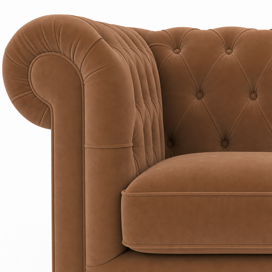 Close-up of a classic Chesterfield armchair in warm camel brown velvet, showing the tufted backrest, rolled armrest, and cushion on a white background.