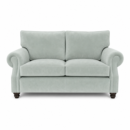 A classic two-seater loveseat sofa upholstered in a light sage green velvet fabric, featuring rolled arms, dark wooden feet, and a clean silhouette on a white background.