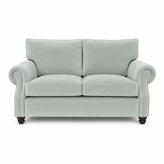 A classic two-seater loveseat sofa upholstered in a light sage green velvet fabric, featuring rolled arms, dark wooden feet, and a clean silhouette on a white background.
