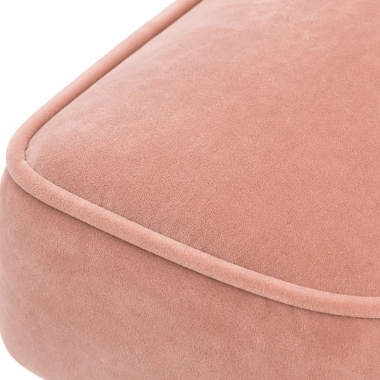 Close-up of a dusty pink velvet or velour upholstered cushion corner with a rounded edge and piping detail, set against a plain white background.