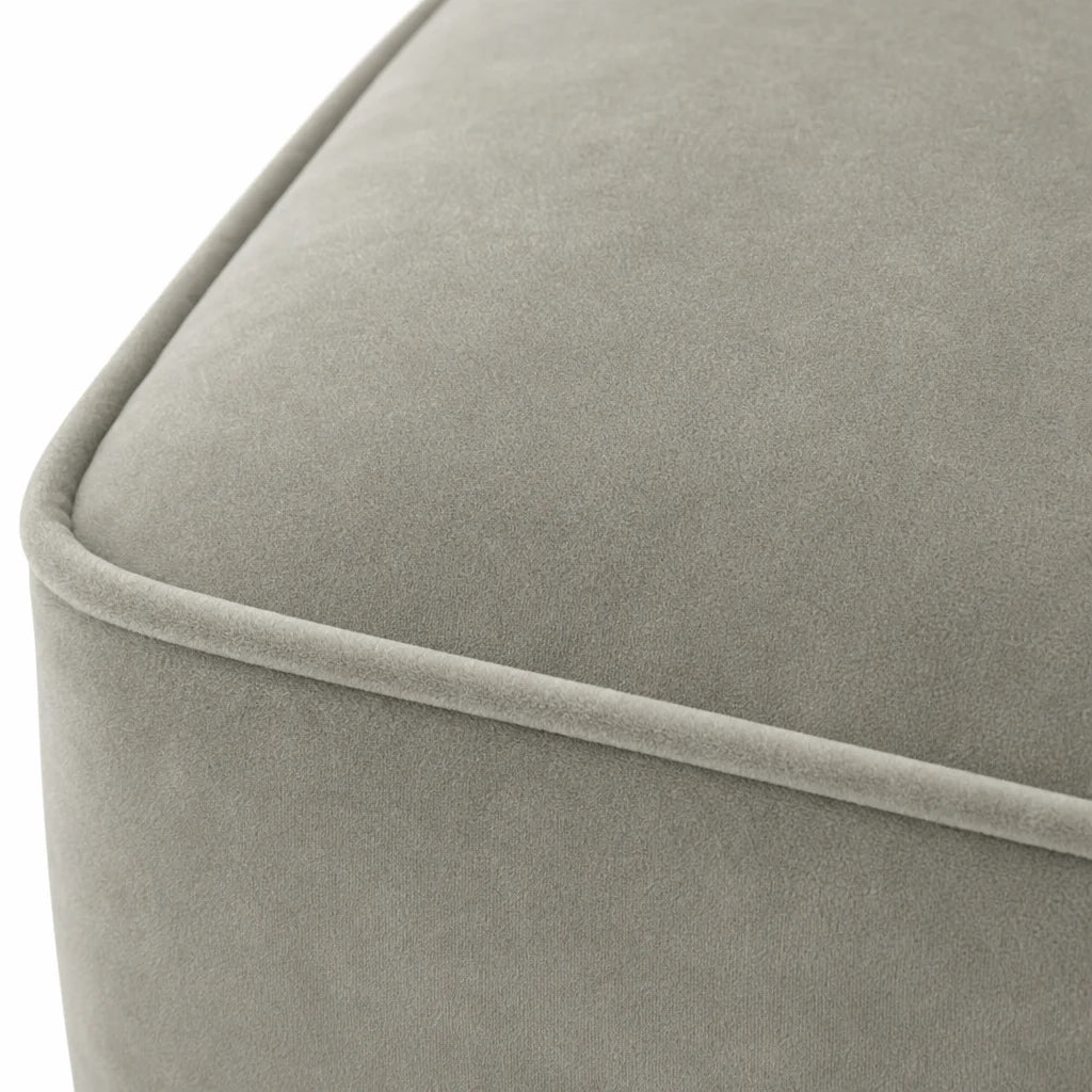 Close-up of a light gray upholstered furniture corner with a soft velvet-like texture and a piped edge, shown against a white background.