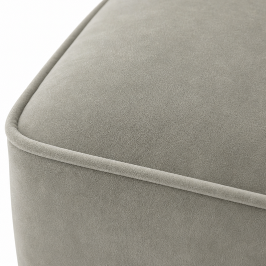 Close-up of a light gray upholstered furniture corner with a soft velvet-like texture and a piped edge, shown against a white background.