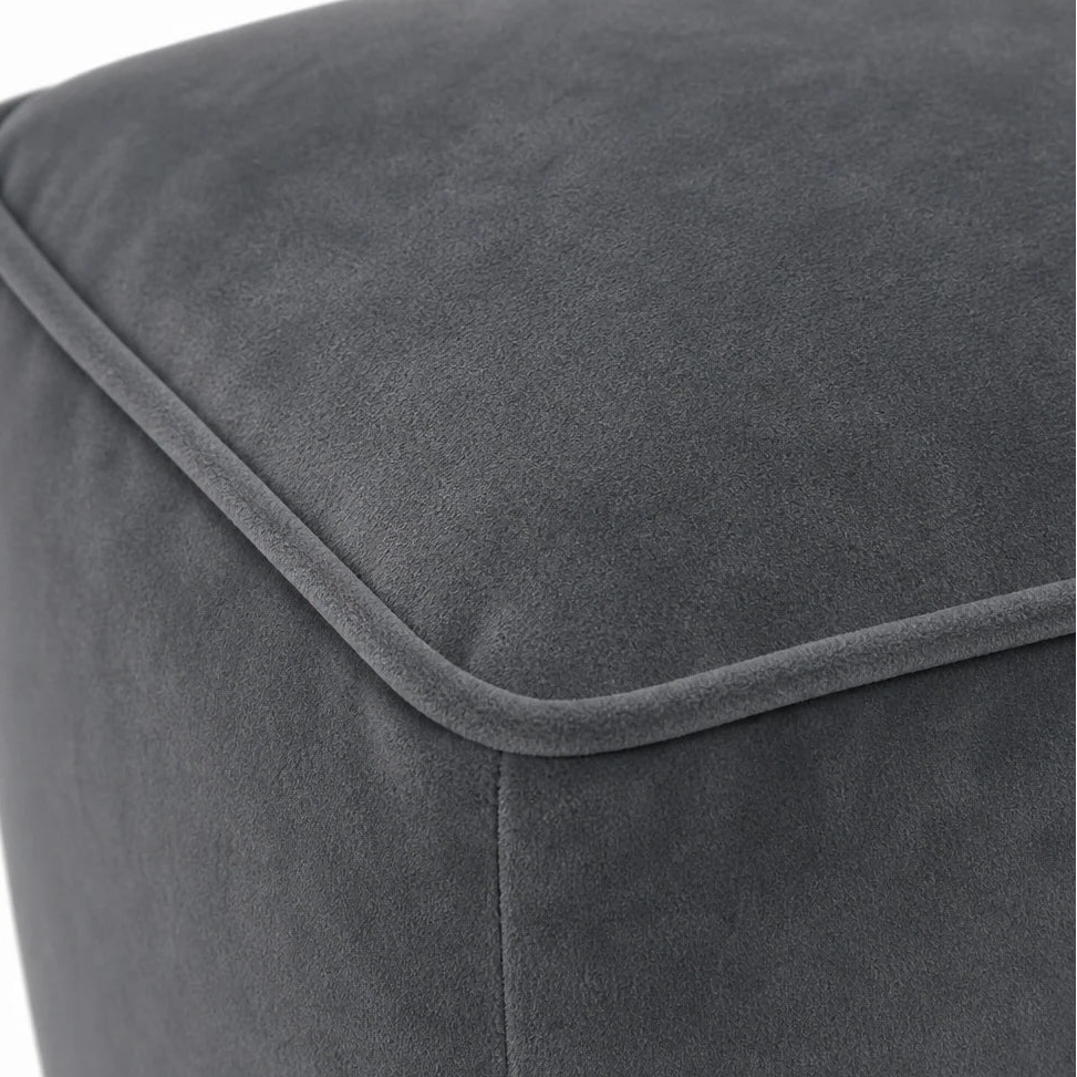 Close-up of a dark gray upholstered ottoman or pouf, showing the fabric texture and stitched corner seam against a white background.