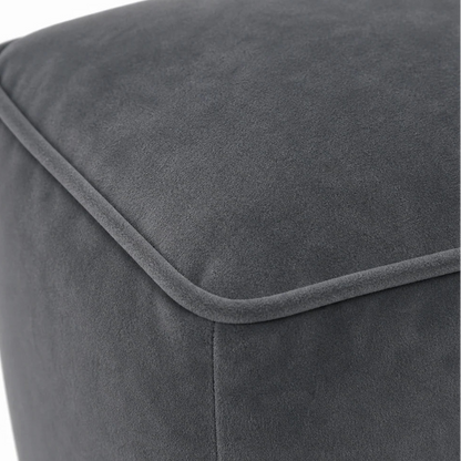 Close-up of a dark gray upholstered ottoman or pouf, showing the fabric texture and stitched corner seam against a white background.