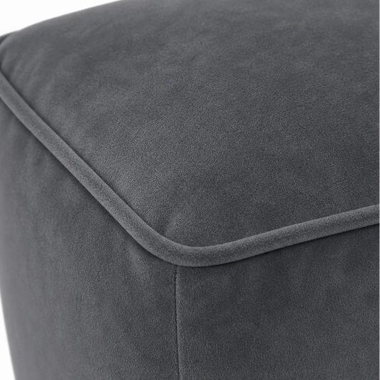 Close-up of a dark gray upholstered ottoman or pouf, showing the fabric texture and stitched corner seam against a white background.
