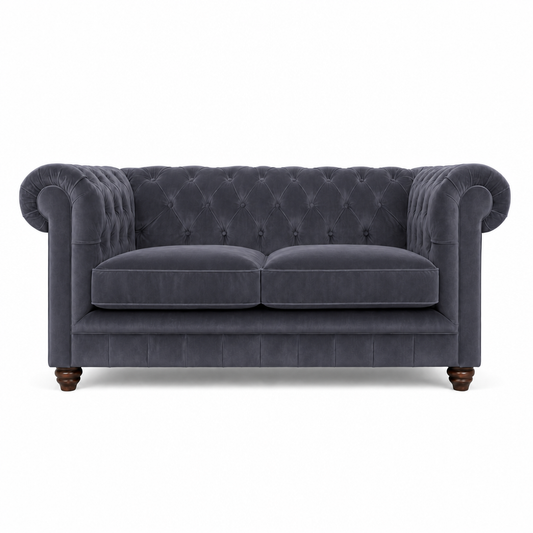 A classic Chesterfield loveseat sofa upholstered in dark slate blue velvet, featuring a tufted button backrest, rolled arms, two seat cushions, and dark wooden turned legs, shown against a plain white background.