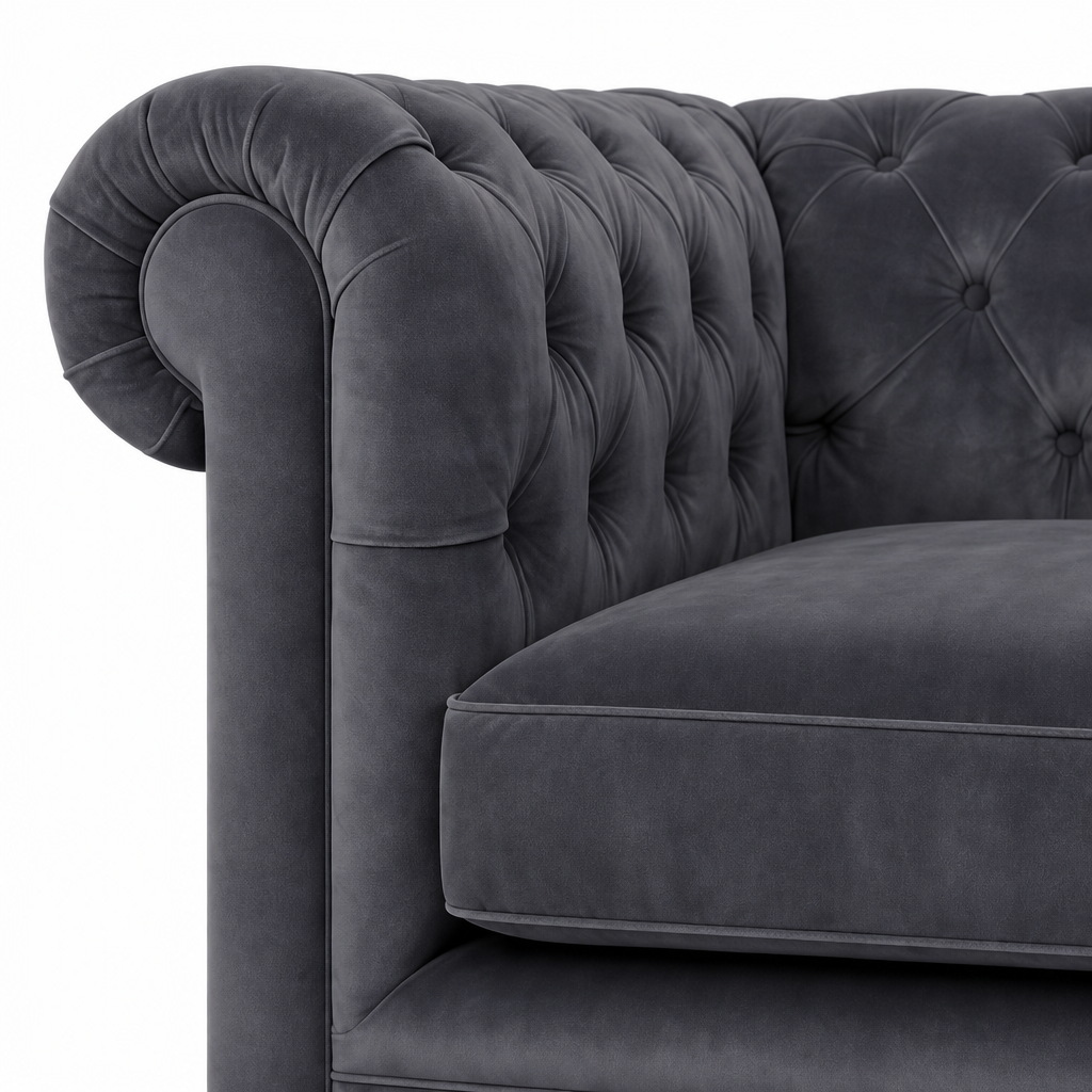 Close-up of a dark gray velvet Chesterfield armchair showing the tufted backrest, rolled armrest, and cushion on a white background.