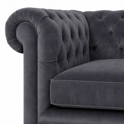 Close-up of a dark gray velvet Chesterfield armchair showing the tufted backrest, rolled armrest, and cushion on a white background.
