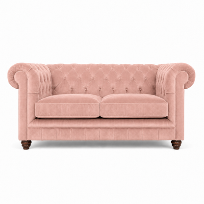 A classic Chesterfield-style loveseat sofa upholstered in dusty pink velvet, featuring a tufted backrest, rolled arms, two seat cushions, and dark wooden legs, shown against a plain white background.