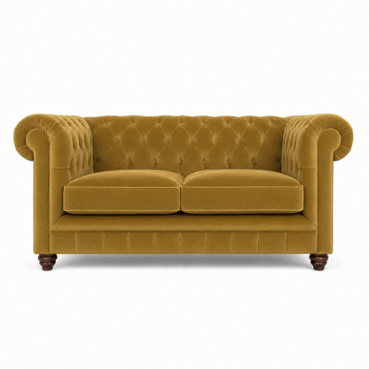 A classic Chesterfield loveseat sofa upholstered in mustard yellow velvet, featuring a tufted diamond pattern on the backrest and seat, rolled arms, two loose seat cushions, and dark wooden legs, shown against a plain white background.