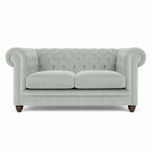 A classic Chesterfield loveseat sofa upholstered in a light blue velvet fabric, featuring tufted button detailing on the backrest and arms, two loose seat cushions, and dark brown turned wood legs, shown against a plain white background.