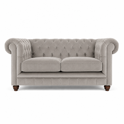 A classic Chesterfield loveseat sofa upholstered in light gray fabric, featuring a tufted diamond pattern on the backrest and seat, rolled arms, two loose seat cushions, and dark wooden legs, shown against a plain white background.