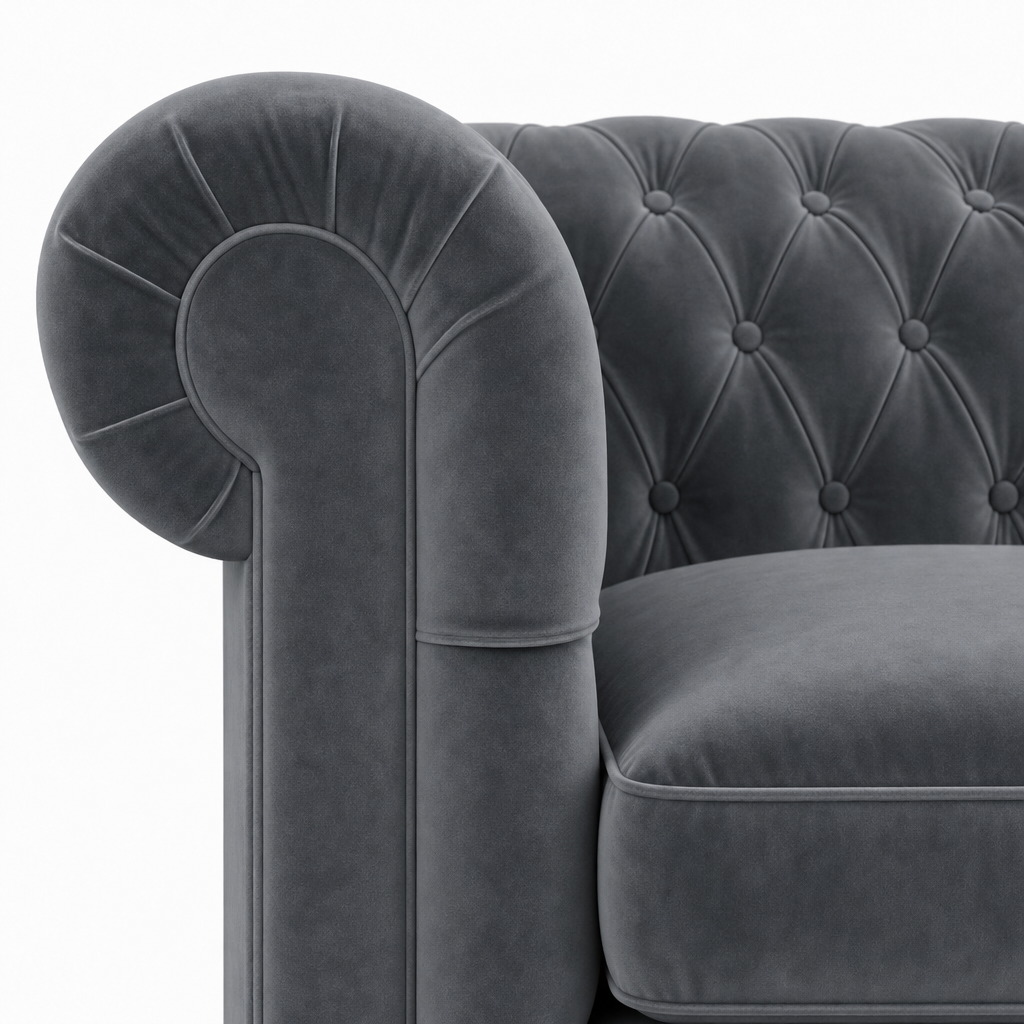 Close-up of a dark gray velvet Chesterfield armchair showing the tufted backrest and rolled armrest against a white background.