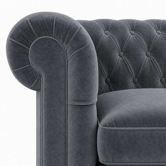 Close-up of a dark gray velvet Chesterfield armchair showing the tufted backrest and rolled armrest against a white background.