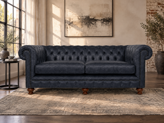 A navy blue tufted velvet loveseat sofa with rolled arms and wooden legs, positioned on a distressed beige rug in a styled living room setting.