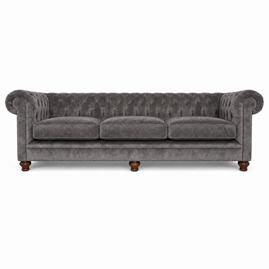 A classic Chesterfield-style three-seater sofa upholstered in textured gray velvet, featuring rolled arms, deep button tufting, three loose seat cushions, and dark wooden legs, shown against a plain white background.