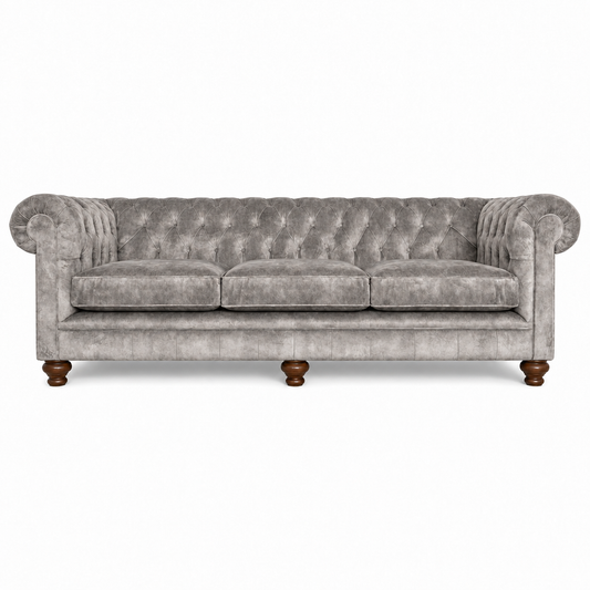 A classic Chesterfield-style three-seater sofa upholstered in textured gray velvet, featuring deep button tufting, rolled arms, and dark brown turned wooden legs, shown against a plain white background.
