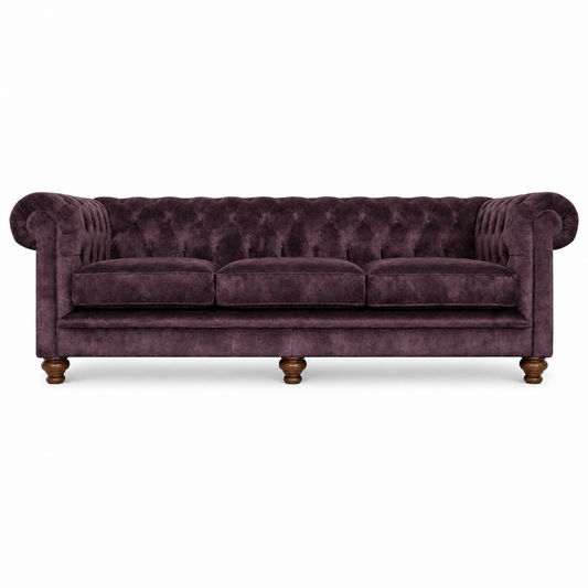 A classic Chesterfield-style sofa upholstered in deep plum purple velvet, featuring tufted button detailing, rolled arms, three seat cushions, and turned wooden legs, shown against a plain white background.