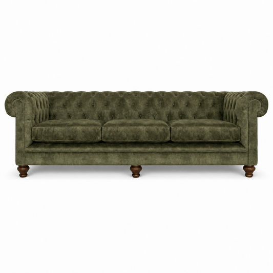 An olive green velvet Chesterfield sofa with tufted backrest, rolled arms, three seat cushions, and dark brown wooden legs, shown against a plain white background.