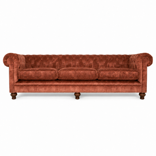 A classic Chesterfield-style sofa upholstered in a rich rust-orange velvet fabric, featuring rolled arms, deep button tufting, three loose seat cushions, and turned wooden legs, shown against a plain white background.
