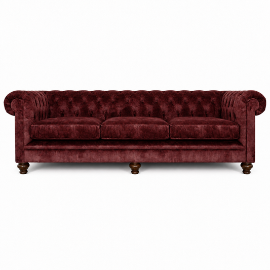 A classic Chesterfield-style three-seater sofa upholstered in deep burgundy velvet, featuring a tufted backrest, rolled arms, three loose seat cushions, and dark wooden turned legs, shown against a plain white background.