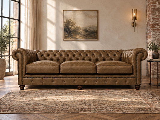 A brown tufted leather Chesterfield sofa in a beautifully styled living room with a patterned area rug, wooden floors, a brick column, and a wall-mounted light fixture.