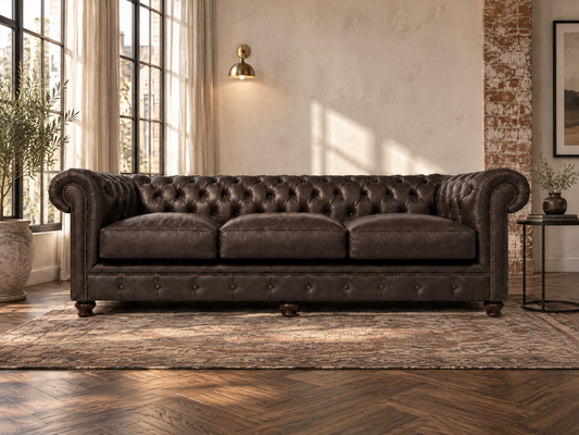 A dark brown tufted leather Chesterfield sofa in a styled living room with a patterned rug, wood herringbone floor, and a warm brass wall sconce.