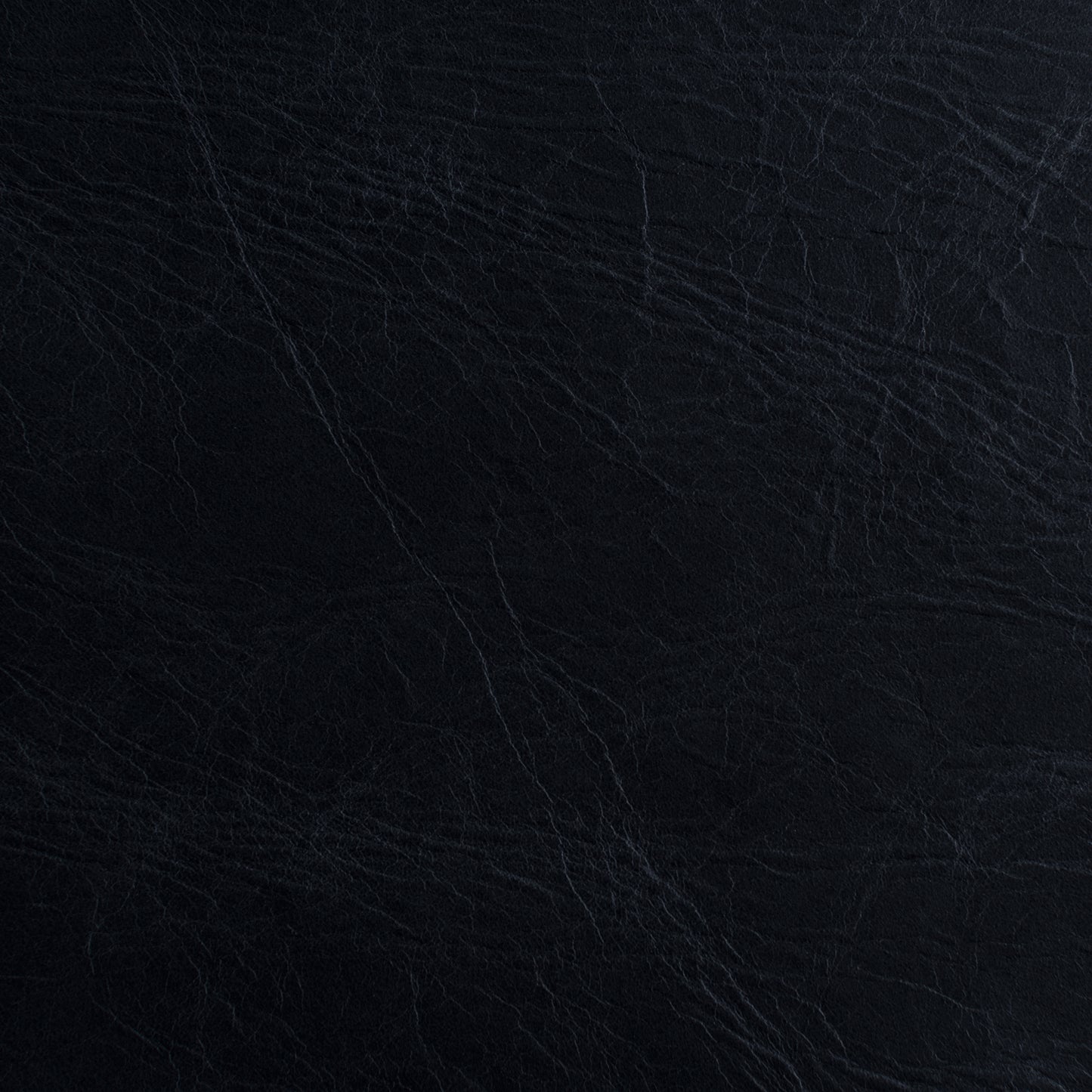 A close-up of a dark textured material, appearing as black leather or faux leather with subtle grain and fine creases.
