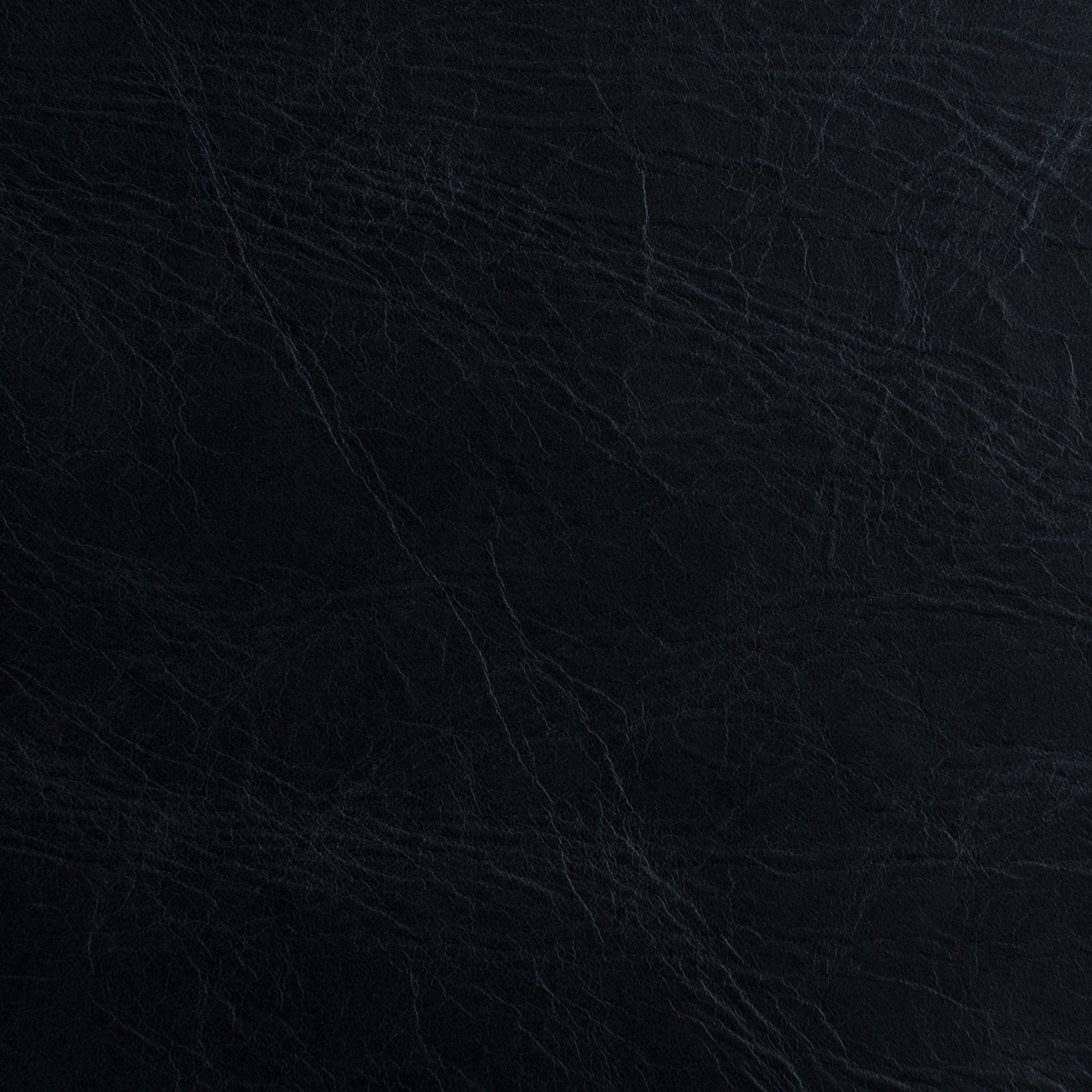A close-up of a dark textured material, appearing as black leather or faux leather with subtle grain and fine creases.